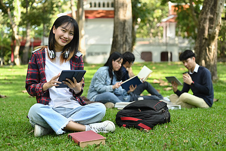 性格开朗的亚洲女学生在校园的绿色草地上使用数字平板电脑 教育 青年和社区概念图片