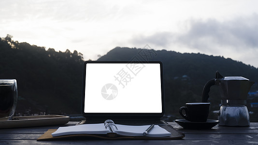 电脑平板电脑 笔记本 莫卡锅和木制桌上的咖啡杯 以山为背景图片
