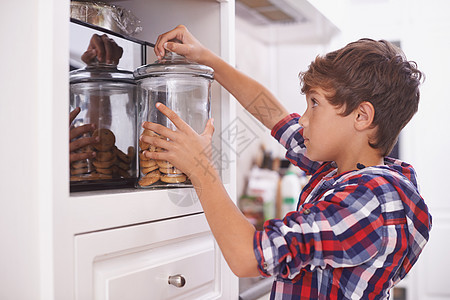 一个男孩在厨房顶层的橱柜里 伸手拿一个饼干罐子 我正想着图片