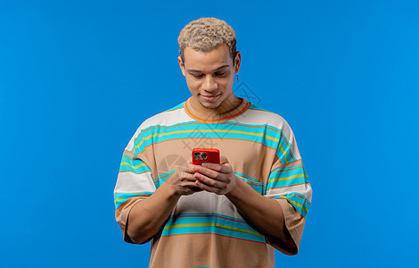 英俊的男性少年在智能手机上上网 在蓝色背景上带着微笑和喜悦的人 科技 成功 幸福 社交网络概念图片