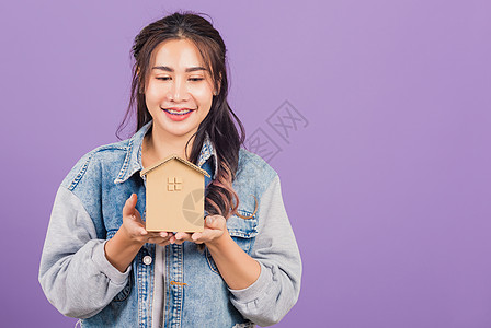 女性戴戴迪尼姆兴奋的笑笑着手握持房屋模型家庭贷款紫色牛仔布成功住宅女士商业现金银行图片