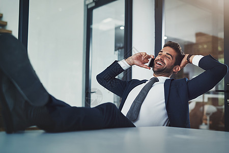 一通电话赚几百万 一位英俊的年轻商务人士在使用手机时双脚放在办公桌上放松黑发办公室男人人士商务套装微笑工作公司生意图片