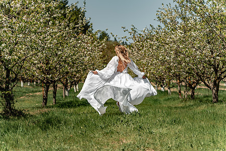 穿着白裙子的女人穿过开花的樱桃园 长裙飞向两侧 新娘一生都欢欣鼓舞 笑声女孩樱花场地晴天乐趣婚礼树木跑步果园公园图片