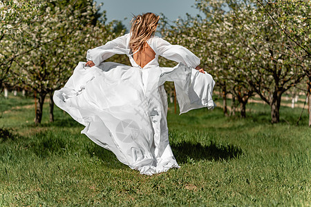 穿着白裙子的女人穿过开花的樱桃园 长裙飞向两侧 新娘一生都欢欣鼓舞 笑声樱花公园自由乐趣果园婚礼跑步场地女士女孩图片
