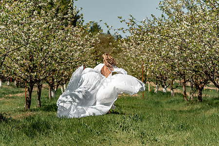 穿着白裙子的女人穿过开花的樱桃园 长裙飞向两侧 新娘一生都欢欣鼓舞 笑声女士晴天乐趣自由头发樱花公园跑步树木场地图片