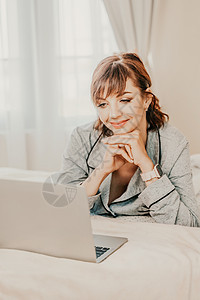 自由职业女性穿着睡衣 躺在床上 在笔记本电脑 电脑上工作 在互联网上学习 上网冲浪 放松 放松 在卧室 客厅 家里 酒店房间里度图片