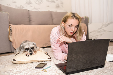 年轻女子正在笔记本电脑上工作 一只灰狗躺在她旁边的地毯上图片