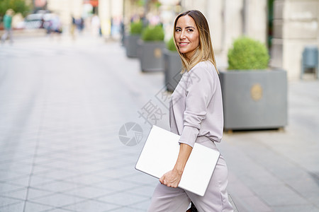 在开会前在街上走着笔记本电脑的快乐女经理图片