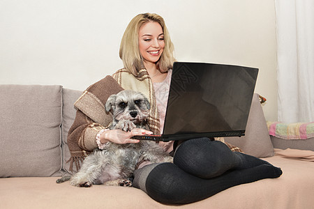 可爱的女士微笑和拥抱 在沙发上一个可爱的狗 同时在笔记本电脑上看电影图片