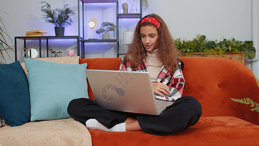 女孩坐在家沙发上 看着照相机 与朋友或家人进行视频会议电话女性公寓孩子电脑博主博客童年技术孩子们老师图片