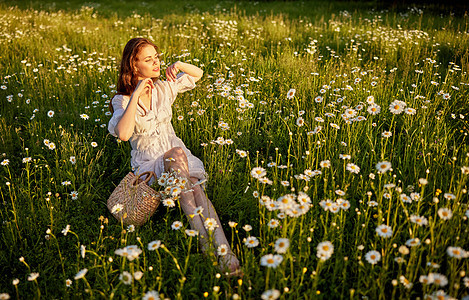一位穿着轻礼服的美丽的女士坐在甘菊花田里成人洋甘菊公园幸福雏菊女性女孩晴天日落场地图片