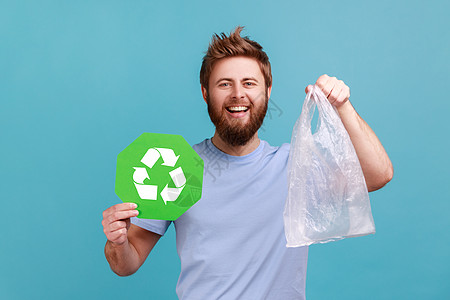 穿着T恤的人拿着绿色回收标志和塑料袋 带着愉快的笑容看着照相机图片
