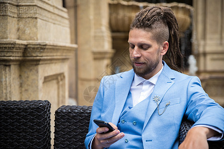穿着蓝西装的年轻成功男子 坐在豪华街咖啡厅里 看着智能手机图片