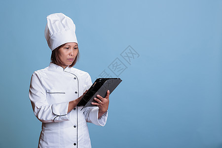 配有围裙和白制服的严肃厨师 手持平板电脑浏览烹饪食谱图片