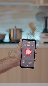坐在厨房里的男性拿着带照明控制应用程序的手机自动化界面软件经济房子监控屏幕技术房间互联网图片