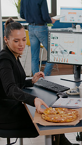 中午休息的女商务人士在餐桌上吃饭吃披萨快餐纸袋职场咖啡送货邮递员数据企业家图表电脑人士图片