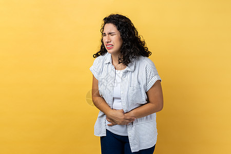 站着不健康的妇女 用手 腹部抽筋或周期疼痛抱住她的肚子图片