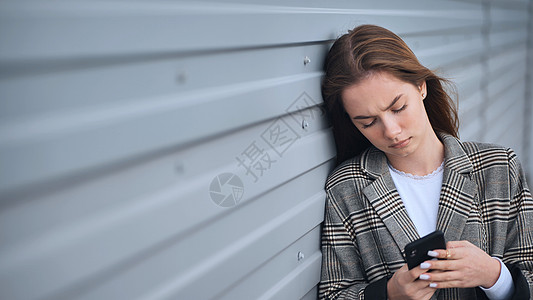 一个心怀不满的女孩 盯着一个智能手机对着一堵条纹墙学生孤独新闻女士电话社交黑眼睛不满女性头发图片