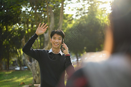 在校园里微笑的年轻男子 手举起手来向朋友问好图片