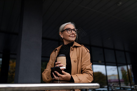 成年灰色头发的天主教女商务人士 外边一座灰色大楼附近有一杯咖啡图片