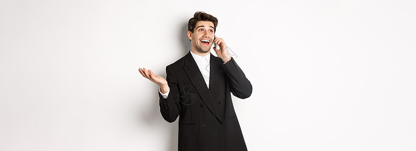 快乐帅气商务人士的肖像 他收到了很好的报价 在电话里聊天 看起来很高兴 站在白色背景下的黑色西装成功人士员工网络手机技术房地产办图片