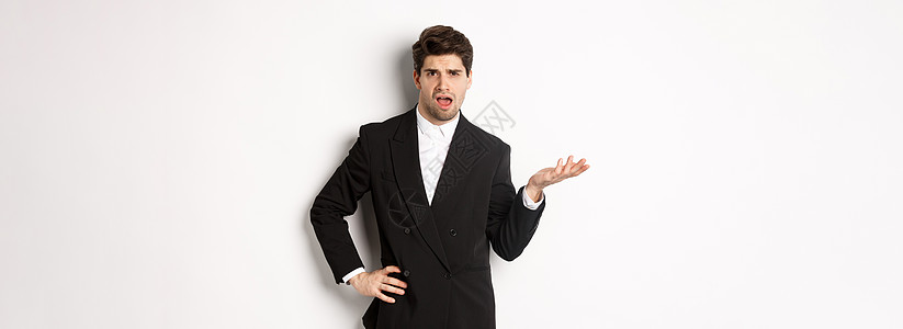 穿着黑西装的自大男子的肖像 看着困惑和失望 抱怨一些奇怪的事情 站在白色背景上站立促销手势人士标识经理老板购物办公室金融套装图片