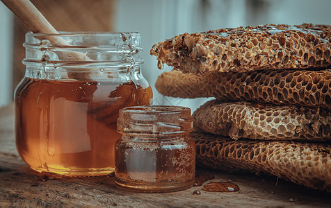 从玻璃罐上的新鲜蜂窝里滴的美味蜂蜜 和老木制桌子上的伍德蜂蜜配方棒糖浆琥珀色饮食香气玻璃味道美食食物金子葡萄糖图片