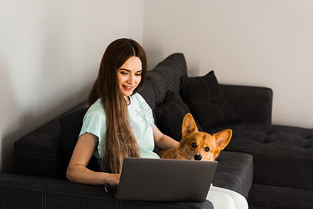 女孩和她的宠物坐在沙发上 一起看笔记本电脑上的电影 与威尔士人的生活方式是一对友谊办公室房子朋友自由职业者教育家庭动物休息公寓图片