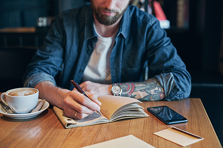 在木制桌子上的笔记本上写笔的人手沉思阅读笔记职场数据教育经理男人咖啡杯子图片