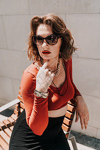 一个女人在街上的画像 外面的长凳上坐着一个戴着眼镜 穿着红色衬衫和黑色裙子的迷人女人人行道衣服头发购物成人姿势冒充腰带身体城市图片