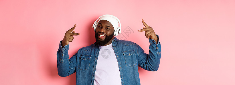 冷酷的非洲  美国男人跳舞嘻哈舞 在耳机里听音乐 站在粉红背景上音乐歌曲购物电话成人衬衫胡须阅读促销快乐图片