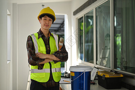 戴安全头盔的画家肖像 手持油漆刷子 站在建筑工地站立 对着镜头微笑图片