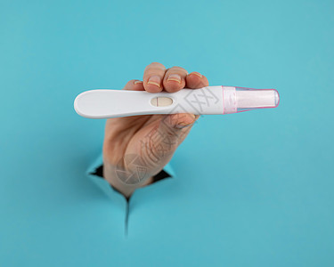 一只用蓝纸板背景的洞露出阴性怀孕测试的手 笑声药物卫生妈妈保健母性生育女孩蓝色条纹生育力图片