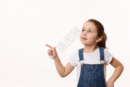可爱的小女孩 穿着蓝色牛仔服的可爱女婴 指着白底幕上的一个广告空间副本图片