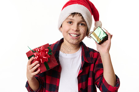 可爱的西班牙裔小男孩戴着圣诞帽 微笑着露出美丽的露齿微笑 摆着圣诞礼物看着镜头图片