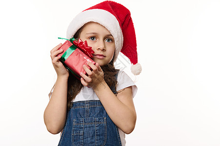 带着圣诞礼物 穿着圣诞帽子的小女孩在白色背景上孤立无援 期待即将到来的冬季节日假期图片