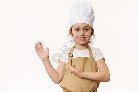 穿着厨师制服的迷人小女孩 对着镜头甜甜地微笑 将她的手指向一个空白的地方 用于广告文字图片