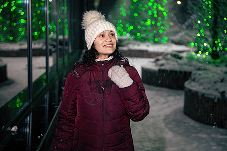 穿着温暖衣服的漂亮女人 在街上走在街上 在一个寒冬雪之夜被花冠照亮图片