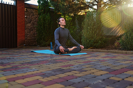 和平男子瑜伽士 运动员在户外莲花姿势中冥想 在日落时练习瑜伽 而太阳光线落在后院图片