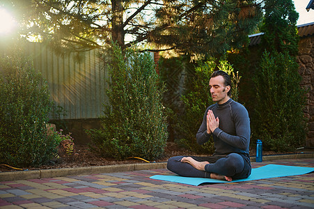 日落的阳光落在后院 而一个男人 瑜伽士在瑜伽垫上以莲花的姿势冥想 双手合十图片