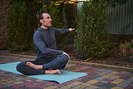 男性运动员在日落时的户外练习中伸展身体 坐在瑜伽垫上的莲花姿势 将手臂伸向两侧图片