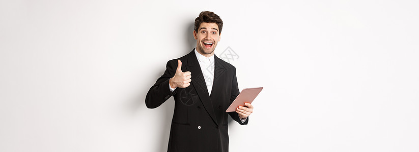 穿着西装的英俊商务人士肖像 举起拇指和赞美 在数字平板上表扬一些东西 站在白背景之上人士工作套装工作室商业广告老板男人经理金融图片