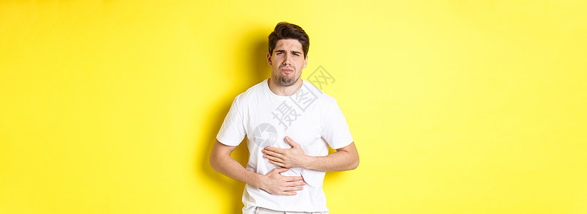 男人肚子痛 痛苦严酷 摸着肚子 站在黄色背景面顶上广告成人工作室学生胡须潮人促销闲暇男性手势图片