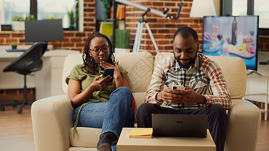 在沙发上一起使用智能手机的非裔美裔夫妇图片