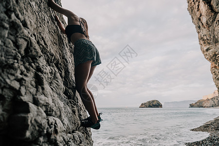 攀登岩石的体育妇女 身材苗条的年轻女子在火山玄武岩洞穴中攀爬 欣赏美丽的海景 女运动员在大自然中训练 女人克服困难的攀登路线冒险图片