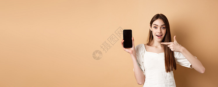 开心的女人对空的电话屏幕指手指尖 看着兴奋 站在蜜蜂背景上伙伴微笑假期示范手机情感女孩褐色技术工作室图片