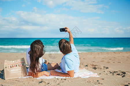 年轻夫妇在海滩上用智能手机自拍图片