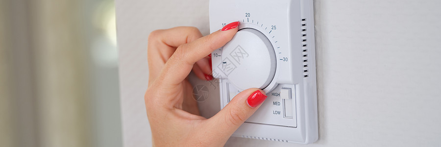 女用手调节自动调温器上住宅中央供暖的温度图片