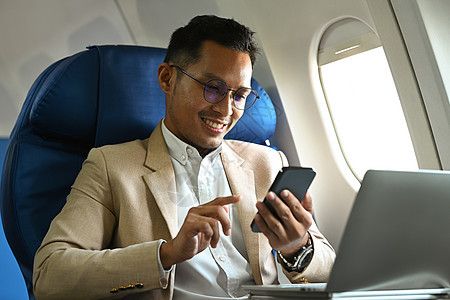 坐在飞机机舱并使用智能电话的千百年商务人士乘客 商业或国外旅行概念;在海外旅游图片