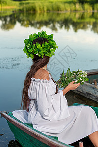 深色头发长发的女神 穿着白色古董礼服 坐在河中央的一条船上若虫冒充女孩花朵神话海滩美人鱼成人魅力魔法图片